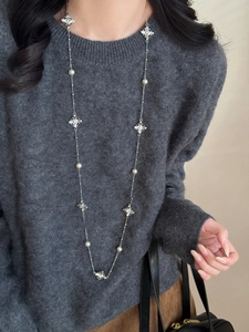 Gros plan du long collier de perles avec des breloques en croix serties de diamants sur tricot