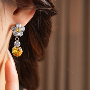Macro shot of silver floral earrings with yellow and white zircon stones on model