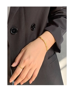 Close-up of a twisted gold vine weave bracelet on a wrist against a dark suit background