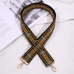 Detail of embroidered geometric bag strap with golden metal hardware and adjustable buckle