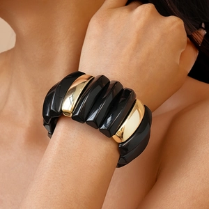 Close-up of a wide elastic bracelet featuring alternating black and gold geometric modules