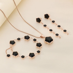 Detail view of a rose gold jewelry set with black clover charms and elegant tassels