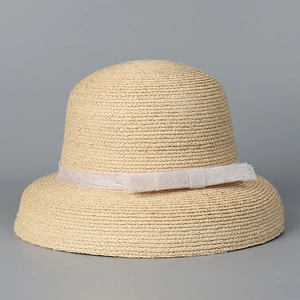 Detail of raffia cloche hat featuring tight woven texture and white lace ribbon bow