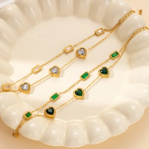 Gold stainless steel bracelet with green gemstones and heart pearls in a white ceramic dish