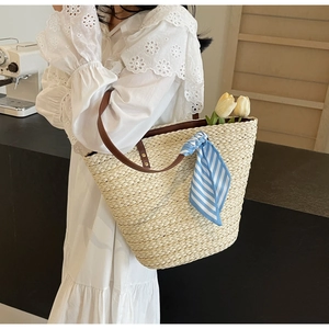 Straw tote bag with brown straps and a blue-white striped scarf for summer beach vacation