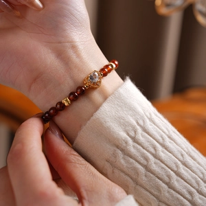 Detail of garnet beaded bracelet with a golden heart pendant worn on a female wrist