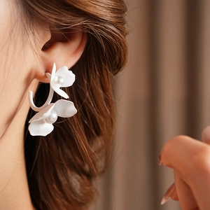 Close-up of elegant C-shaped white floral earrings with pearls worn by a model