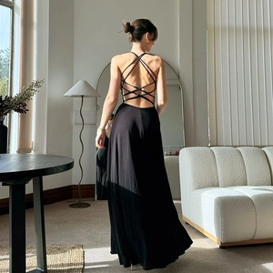 Elegant black backless maxi dress with cross-strap detail in a modern interior setting