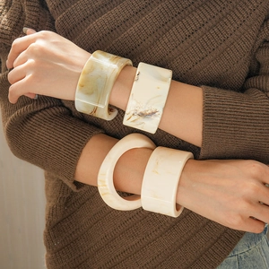Close-up of resin cuff bracelets with marble texture on brown knit sweater background