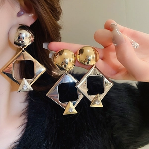 Detailed close-up of geometric gold drop earrings with rhinestone accents on a model