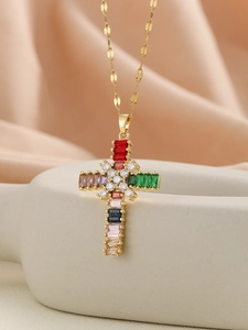 Macro shot of gold cross necklace with colorful rectangular gemstones on pink silk