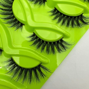 Dramatic cat-eye false eyelashes in a dense, crisscross design on a vibrant green tray