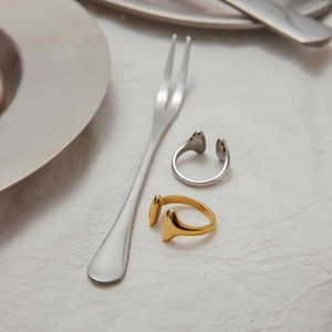 Minimalist gold and silver open rings displayed on white linen with a steel fork