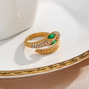 Macro shot of 18K gold snake ring with green crystal eyes and scale texture on silk