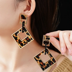 Detail view of rhombic leopard print earrings with gold metallic frames worn by a model