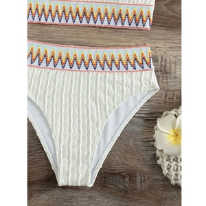 White one-shoulder high-waisted bikini set with colorful bohemian embroidery on wood background