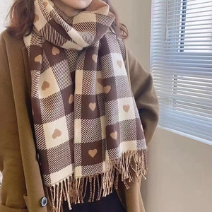 Detail of brown and cream checkered scarf with heart patterns and fringe edges on model