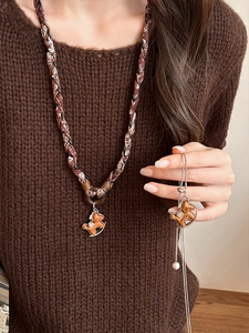 Gros plan du collier vintage cheval en cuir avec perle sur un pull marron chaud