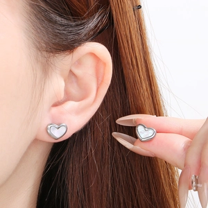 Detail of silver heart earrings with pearl inlay shown on model and held by hand