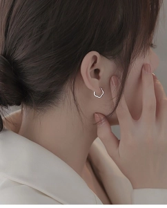 Macro shot of silver hollow wavy hoop earring worn on female model for size detail