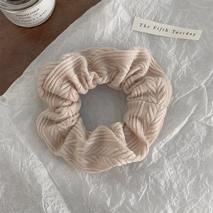 Detail of a beige knitted oversized scrunchie on white paper with an aesthetic candle