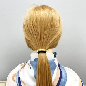 Detail eines goldenen Metall-Haargummis mit schwarzem Elastikband auf blondem Haar