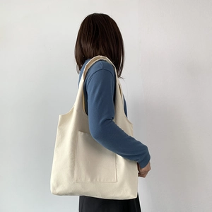 Detail view of off-white canvas tote bag with front pocket shown on a model