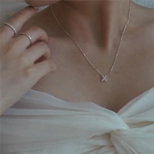 Close-up of a minimalist silver 925 X-shaped cross necklace worn by a model