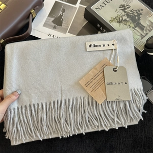 Close-up of light gray knit scarf texture with delicate fringe and premium label detail
