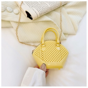 Detail shot of yellow jelly shell bag with gold chain strap on beige knit sweater