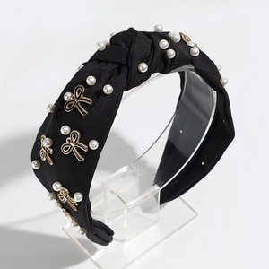 Macro detail of black fabric headband with faux pearls and golden bow accents