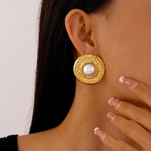 Close-up of vintage gold hammered round earrings with large white pearl on a model