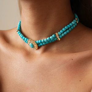 Close-up of double-layer turquoise beaded necklace with gold oval pendant and bow spacers