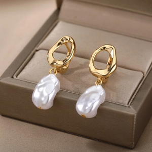 Close-up of golden geometric earrings with white baroque pearls in a beige jewelry box