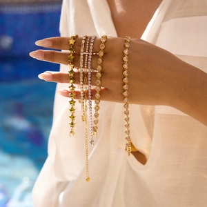 Close-up of gold bracelets with pink and white cubic zirconia on wrist by a pool