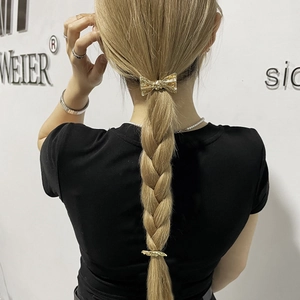 Detail view of golden metal bow hair clip worn on a blonde braid in a minimalist punk style