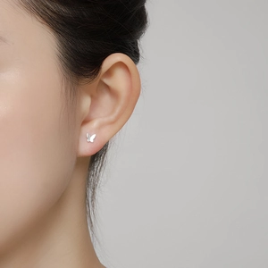 Close-up of elegant silver butterfly stud earrings worn on ear with minimalist style