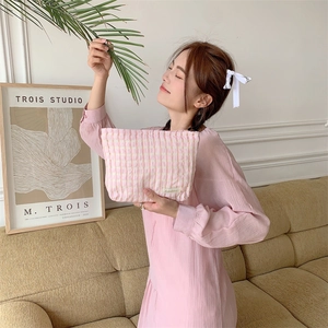 Close-up of pink and white checkered quilted makeup bag held by a person in a cozy room
