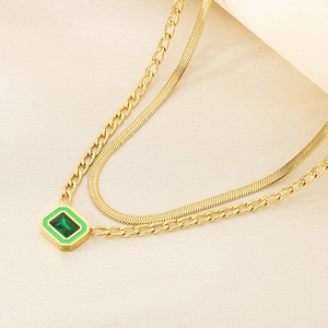 Detail of gold double-layer chain with green gemstone pendant on beige fabric