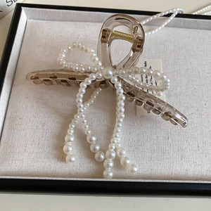 Detailed macro view of champagne bow hair claw clip with white pearl tassels and gold spring