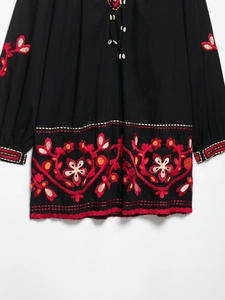 Détail de broderie florale sur robe noire à manches longues avec liens à coquillages