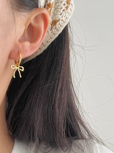 Close-up of a model wearing a gold bow dangle earring made of polished sterling silver
