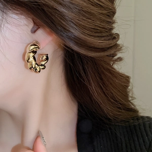 Detail view of a woman wearing a gold-finished metal C-shaped twisted earring