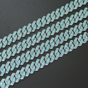 Detail of silver Cuban link chain with paved blue crystals on a dark background