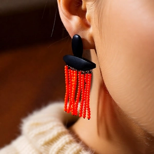 Detail of bohemian long tassel earrings with orange beads and black oval stud worn on ear