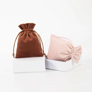Detail of velvet drawstring jewelry pouches in brown and pink on a white gift box
