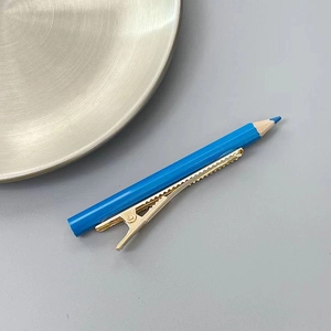 Détail d'une pince à cheveux en forme de crayon bleu avec clip doré sur fond gris