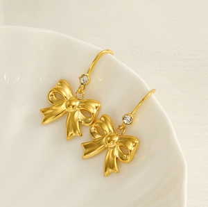 Detailed close-up of gold bow earrings with crystal accents on a ceramic tray