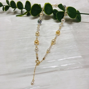 Detailed shot of multi-colored Akoya pearls with a gold lobster clasp on white fabric