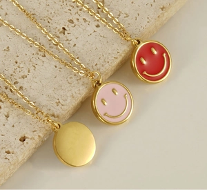 Close-up of three gold stainless steel necklaces with pink and red enamel smiley pendants
